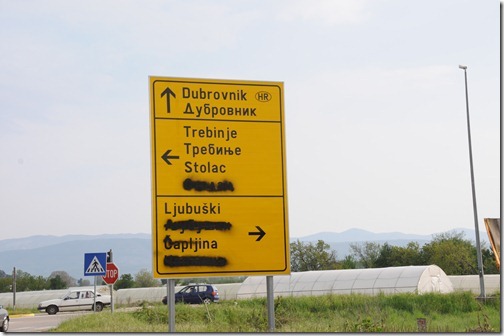 Road sign in Bosnia-Herzegovina, with Cyrillic and Latin Scripts. Note the spraypainted out Cyrillic text, indicating this is a Bozniak area.