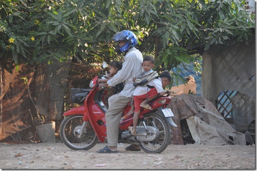 Cambodian motorcycle driver taking three kids for a ride in the countryside near Siem Reap, Cambodia